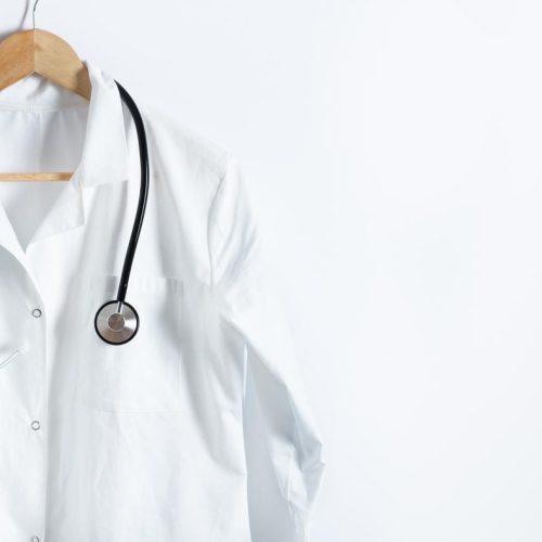 Doctor's white coat with stethoscope on hanger over white background with copy space. Healthcare and medical concept.